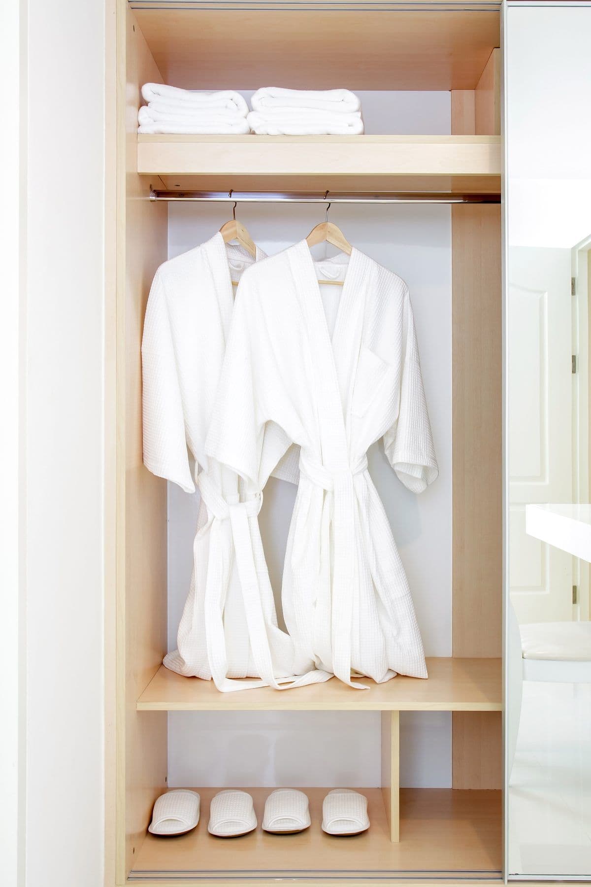 Weiße Bademäntel auf Bügeln in einem Holzschrank